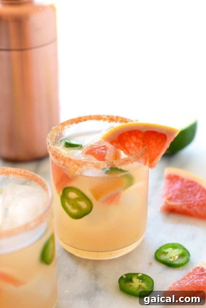Chili-Kissed Grapefruit Margarita 2 Two glasses of spicy grapefruit margaritas garnished with grapefruit slices and jalapeño rounds, ready to be enjoyed.