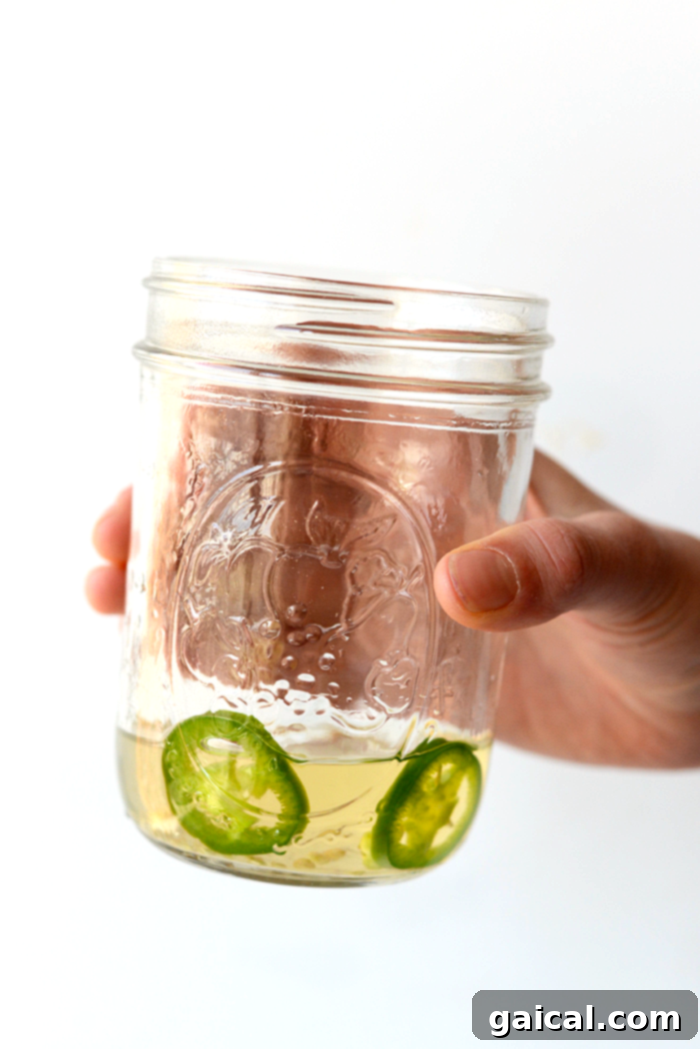 Chili-Kissed Grapefruit Margarita 4 A clear jar filled with tequila and vibrant green jalapeño slices, infusing for a spicy kick.