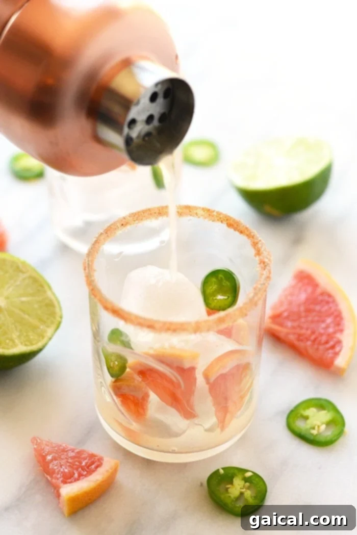 Chili-Kissed Grapefruit Margarita 5 A close-up shot of a single spicy grapefruit margarita, garnished with a lime wedge and a red chili slice.