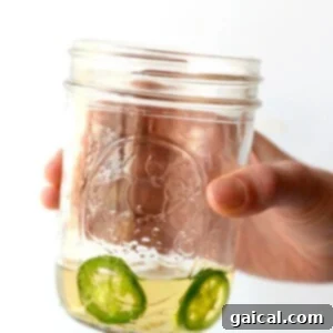 A hand holding a jar of tequila with jalapeño slices in it.