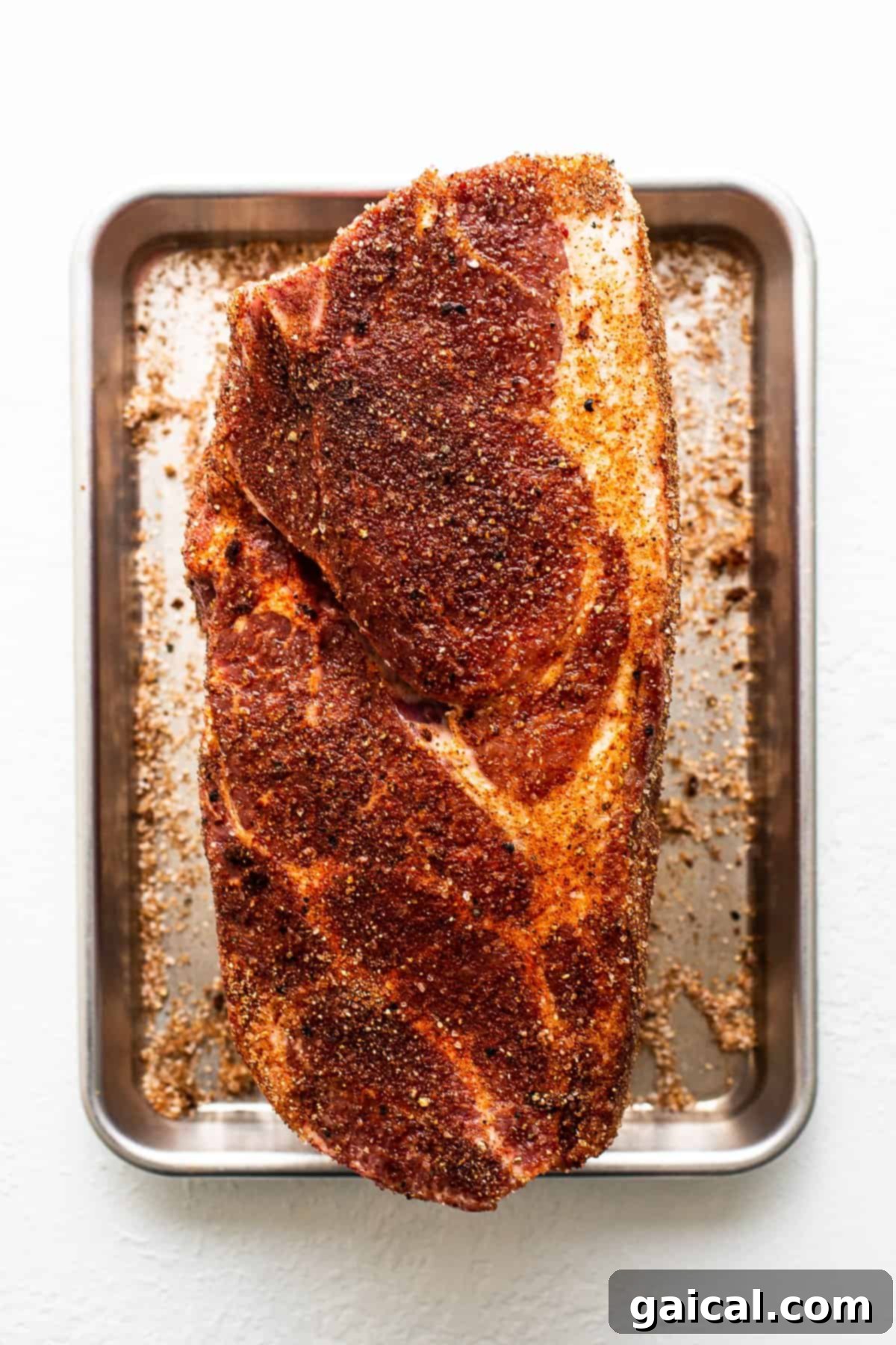 Pork shoulder generously sprinkled with dry rub, ready for smoking.