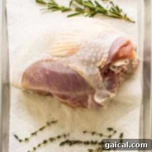 A turkey breast being patted dry with a paper towel on a cutting board.