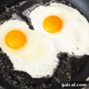 Two eggs are being fried in a frying pan with melted butter.