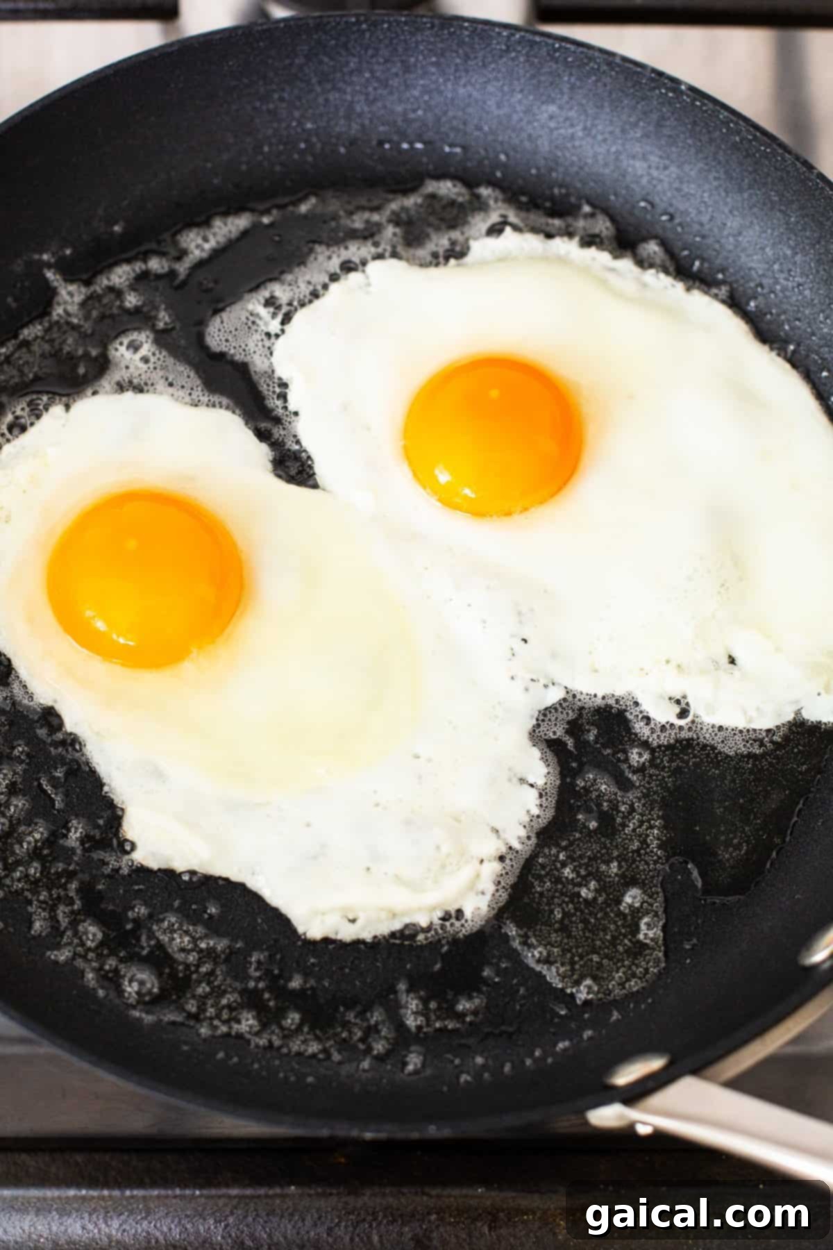 Two eggs frying in a skillet, showing the whites beginning to set for over medium consistency.