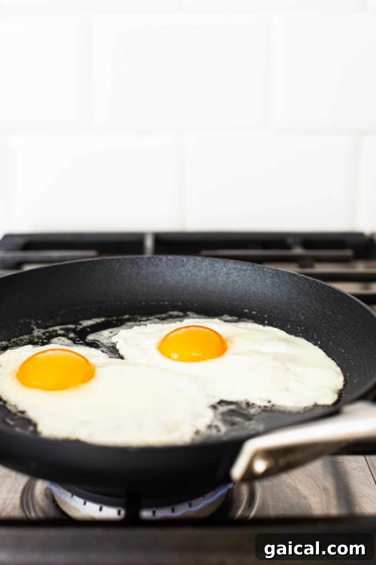 A close-up of over medium eggs frying in a non-stick skillet.