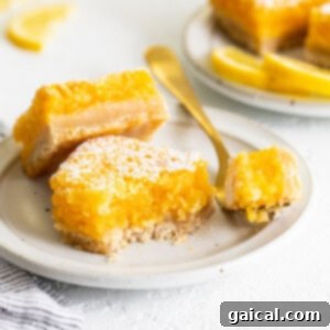 A close-up of a single classic lemon bar, dusted with powdered sugar, on a white plate.