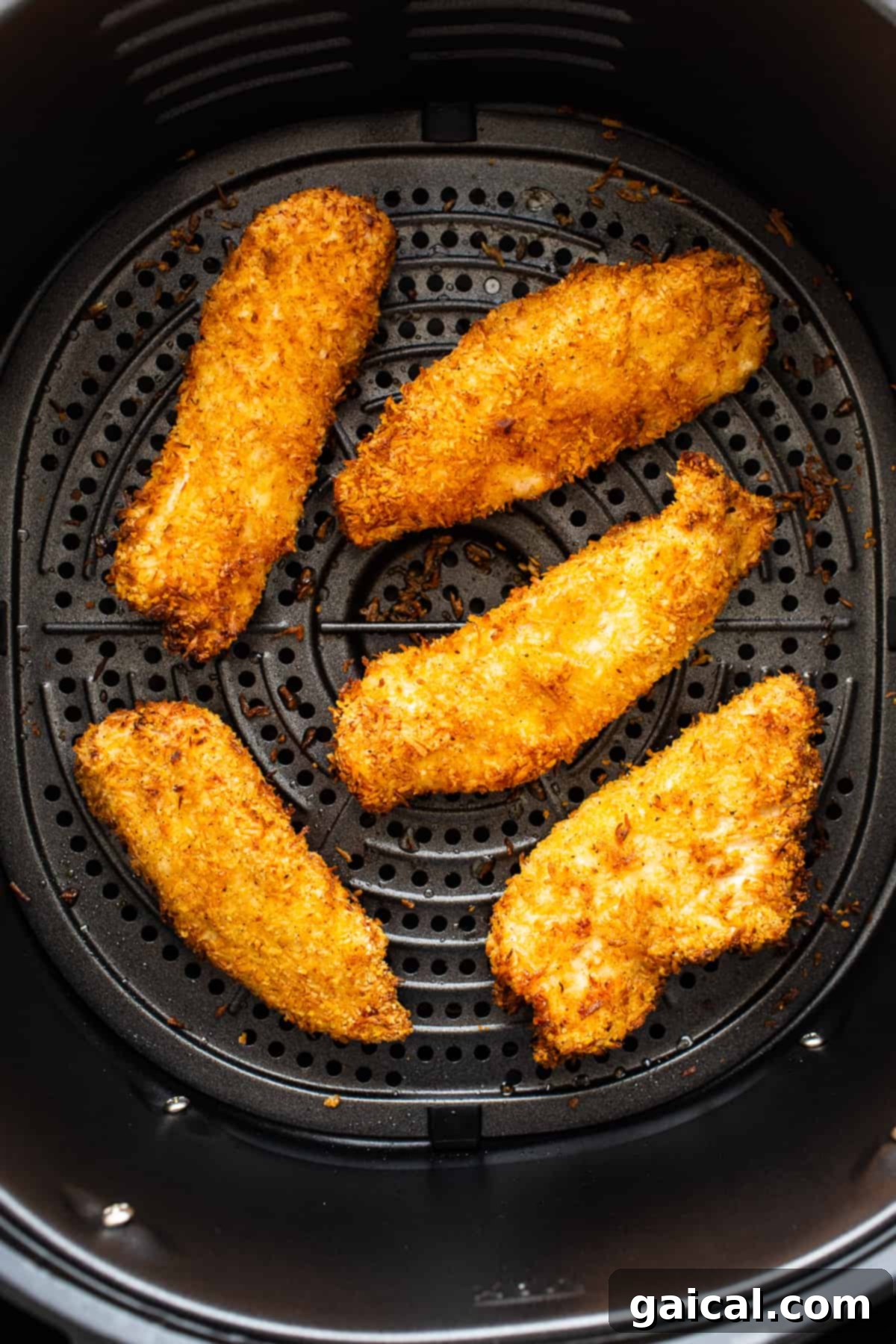 Freshly cooked, golden-brown coconut chicken tenders resting in an air fryer basket, steam visibly rising.
