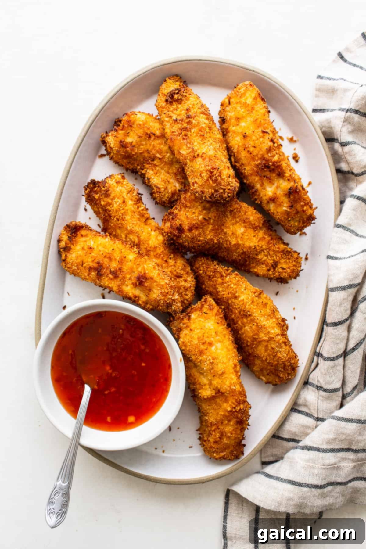 Plated air fryer coconut chicken tenders drizzled with sweet chili sauce, garnished with fresh herbs, ready to be enjoyed.
