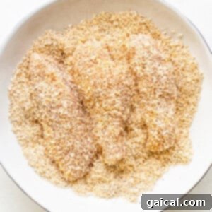 A bowl of breaded raw chicken tenders, coated in coconut and spices.