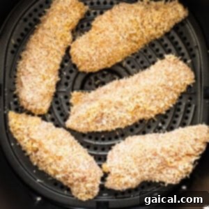 Raw, breaded chicken tenders arranged in a single layer in an air fryer basket, ready for cooking.