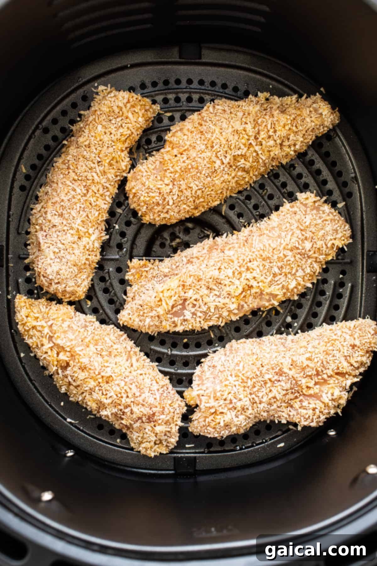 Golden-brown, crispy coconut chicken tenders cooking evenly in the basket of an air fryer, showcasing their delightful texture.