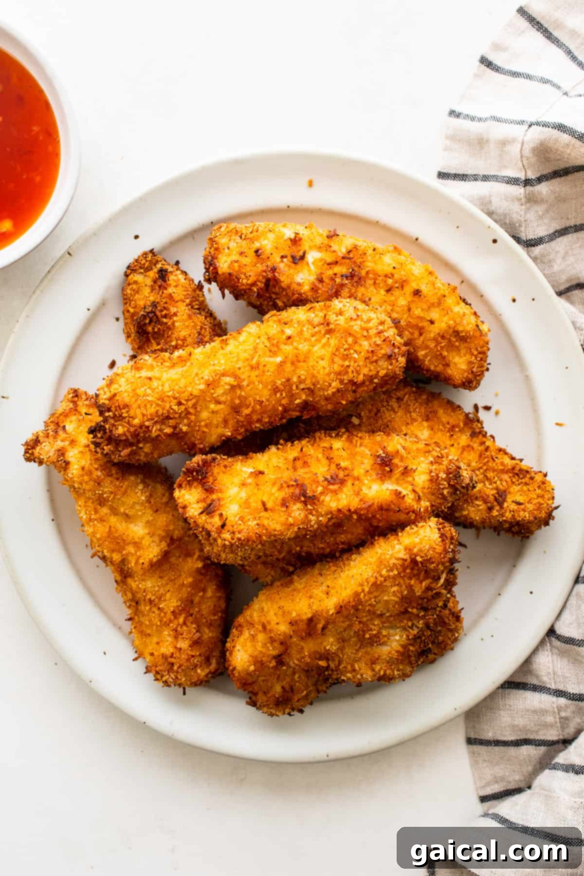 A close-up shot of crispy, golden-brown coconut chicken tenders piled on a white plate, invitingly ready to be served.