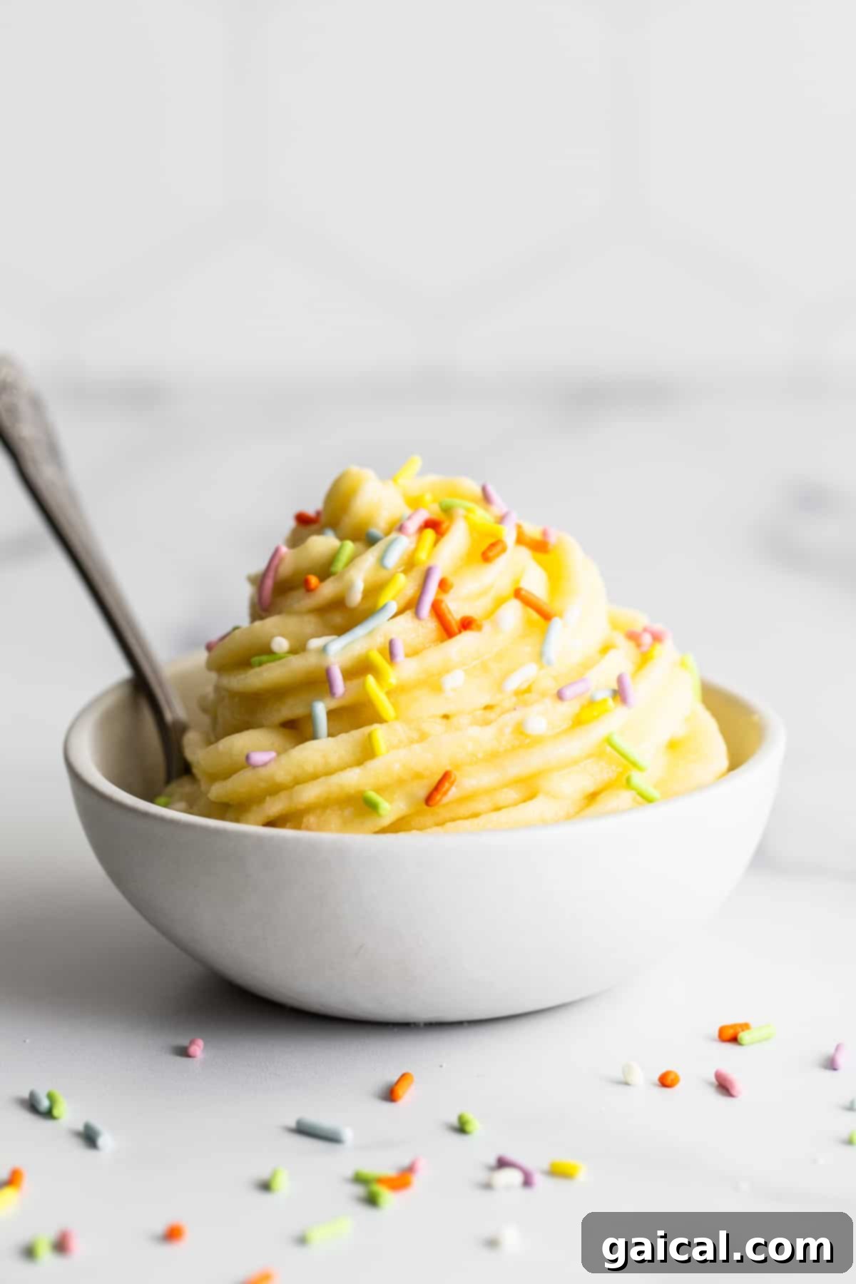 Homemade 4-Ingredient Dole Whip Recipe A vibrant bowl of homemade Dole Whip, perfectly swirled and topped with colorful sprinkles, sitting on a light wooden surface.