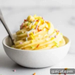 A bowl of creamy, swirled Dole Whip with colorful sprinkles on top, and a spoon resting nearby.