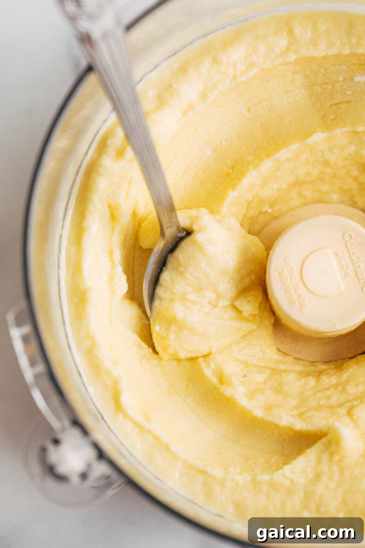 Blending Dole Whip in a Food Processor Creamy pineapple Dole Whip being blended in a food processor, with a spoon resting on the side, showcasing its smooth texture.
