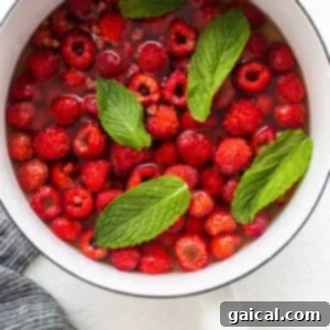 A pan filled with raspberries and mint leaves simmering in honey-infused water, releasing their flavors.