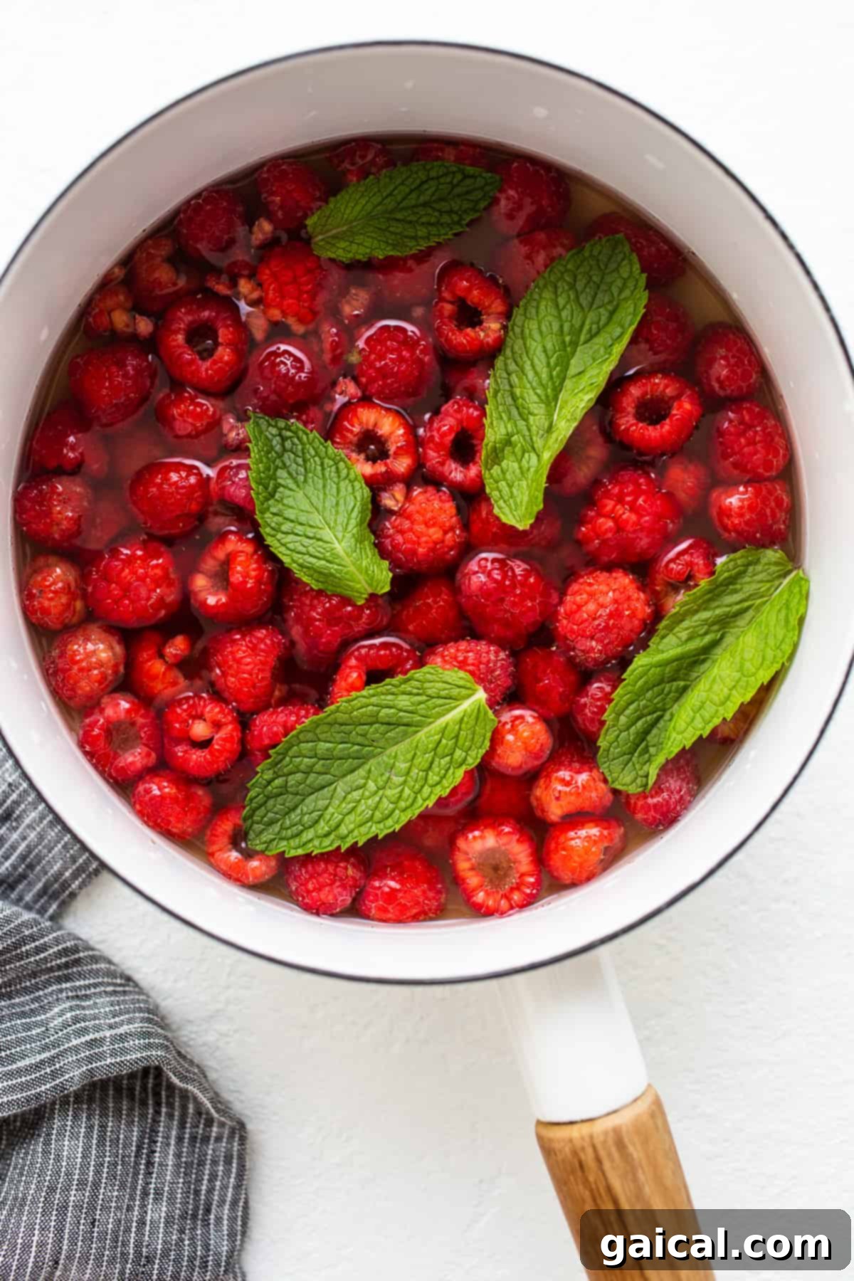 Simmering Raspberries for Homemade Juice Base Fresh raspberries and fragrant mint leaves simmering gently in a saucepan with honey-infused water, creating a vibrant base for a homemade summer punch.