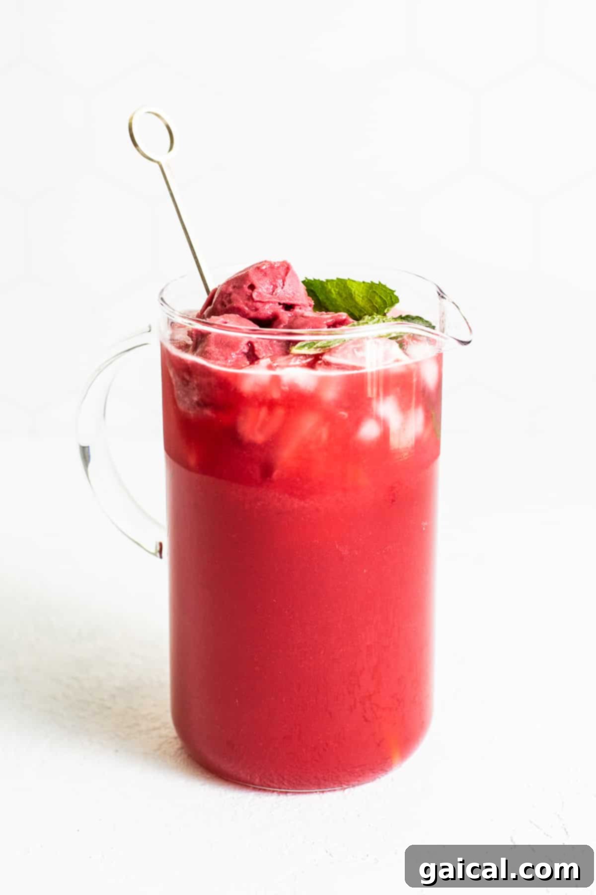 Ready-to-Serve Raspberry Vodka Punch for Your Summer Gathering A large glass pitcher brimming with vibrant raspberry vodka punch, elegantly garnished with fresh mint, basil sprigs, and bright lime slices, perfectly illustrating its refreshing nature.