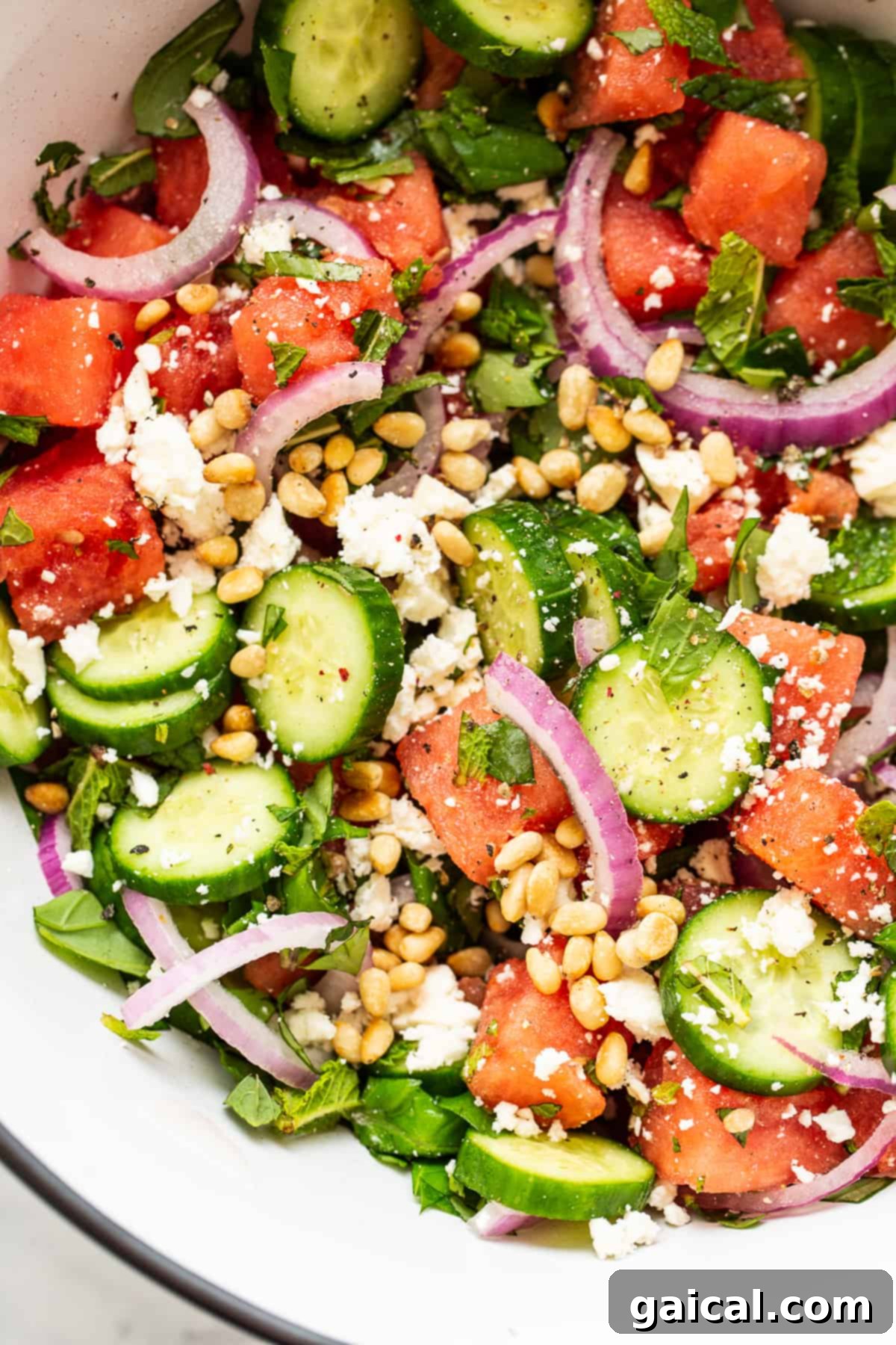 Large bowl of vibrant watermelon feta salad with fresh herbs and pine nuts.