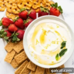 A decorative bowl of fruit dip surrounded by fresh strawberries and crispy crackers on a white plate, ready to be served.