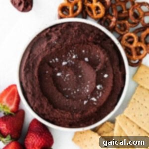 A bowl of rich, edible cookie dough dip sits invitingly next to a pile of crunchy pretzels and juicy strawberries, creating a perfect snack pairing.