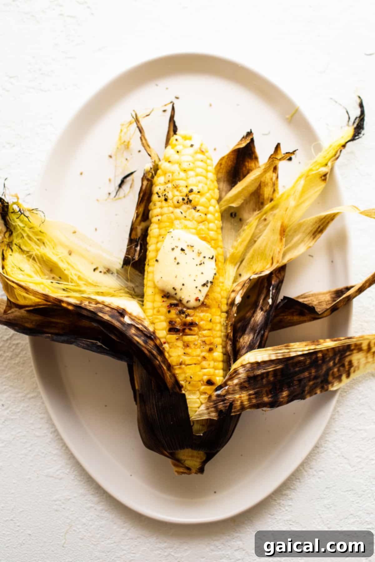 Grilled corn on a plate with melted butter and fresh herbs, ready to be served as a summer side dish.