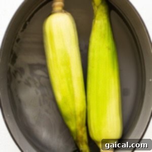 Ears of corn soaking in water in a pot before grilling, preparing for the in-husk method.