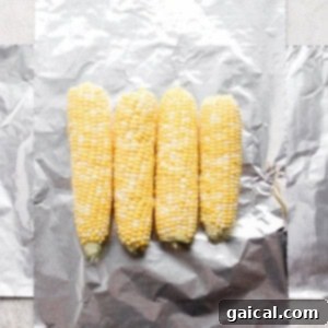 Grilled corn in foil packets on a plate, ready to be unwrapped and served.
