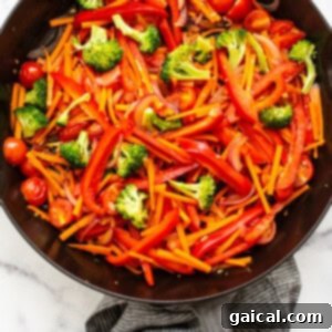Cooking mixed vegetables in a skillet for peanut noodles.