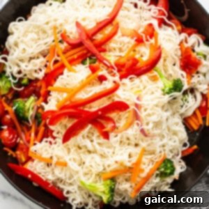 Mixing ramen noodles with colorful vegetables in a large skillet.