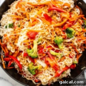 A skillet filled with noodles and vegetables, coated in peanut sauce.