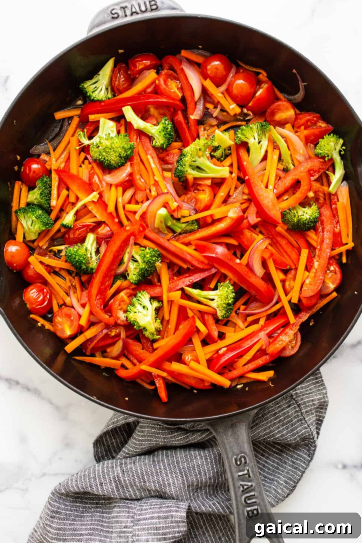 Sautéed Rainbow Vegetables for Noodle Dish A cast iron skillet filled with sautéed vegetables, including sliced red onion, carrots, broccoli, and red bell peppers, glistening with a light sauce.
