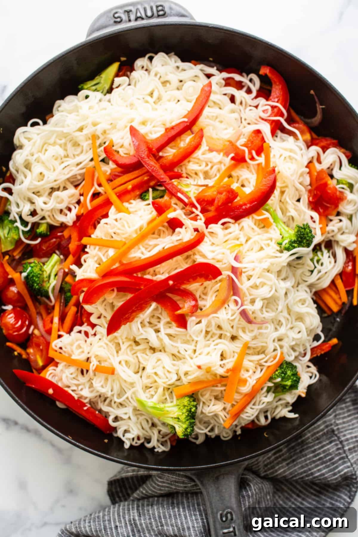 Combining Noodles and Vegetables in Skillet Cooked ramen noodles being tossed with colorful sautéed vegetables in a large skillet, ready for the sauce.