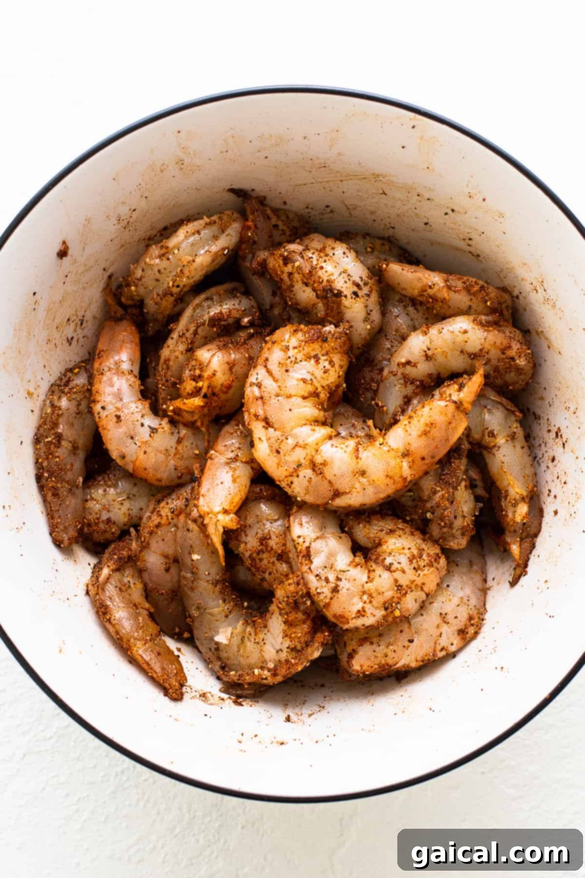 Zesty Shrimp Grill Parcels 5 Raw jumbo shrimp marinated in Old Bay seasoning in a bowl, glistening with spices.