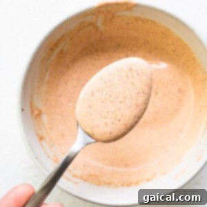 A person holding a spoon full of burger sauce.