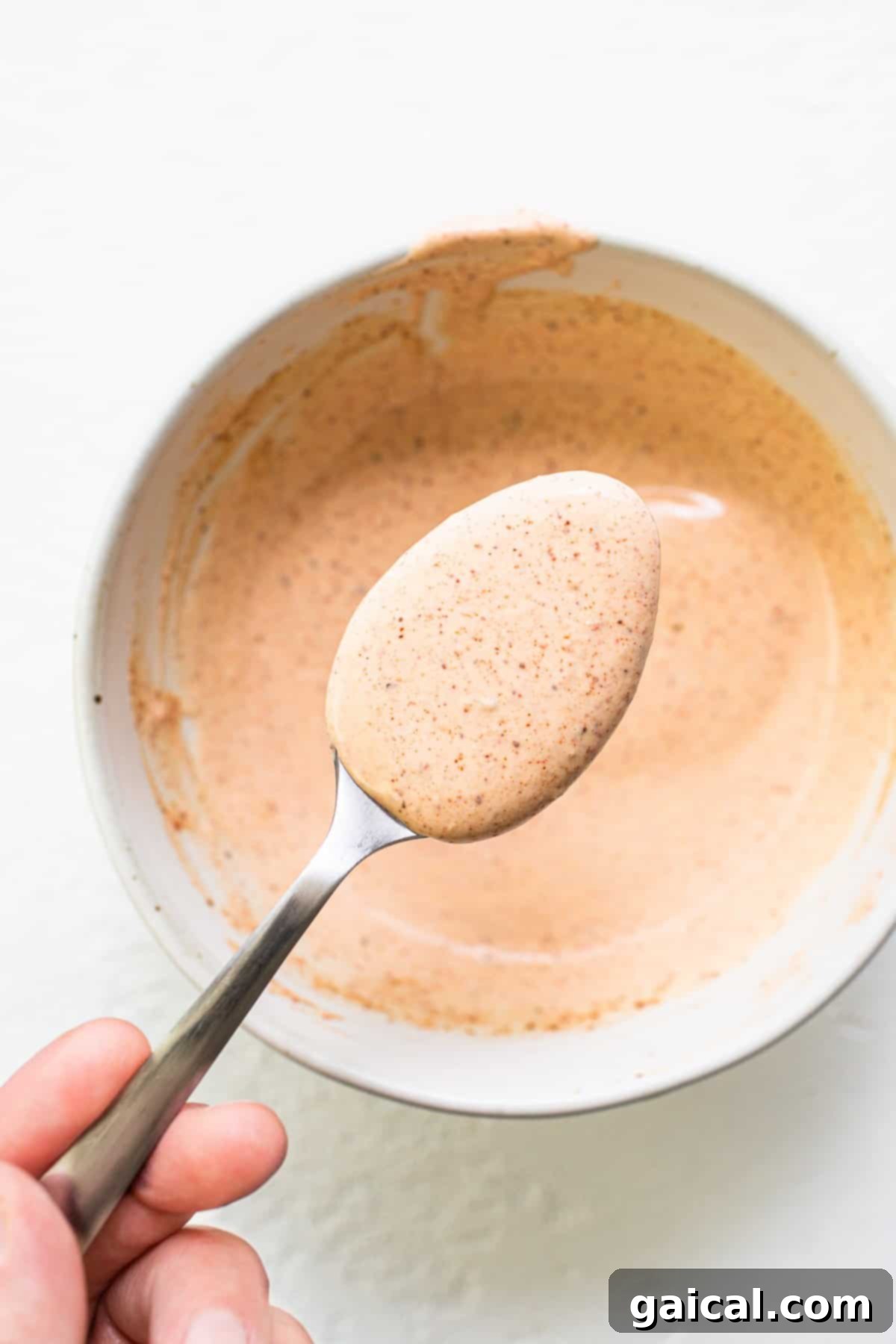 Burger sauce being scooped onto a spoon from a glass bowl.