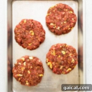 Four beef burgers on a baking sheet.