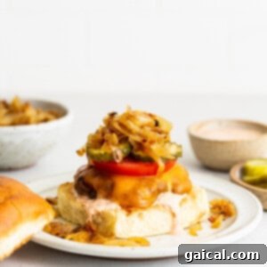 A homemade burger with onions and pickles on a plate.