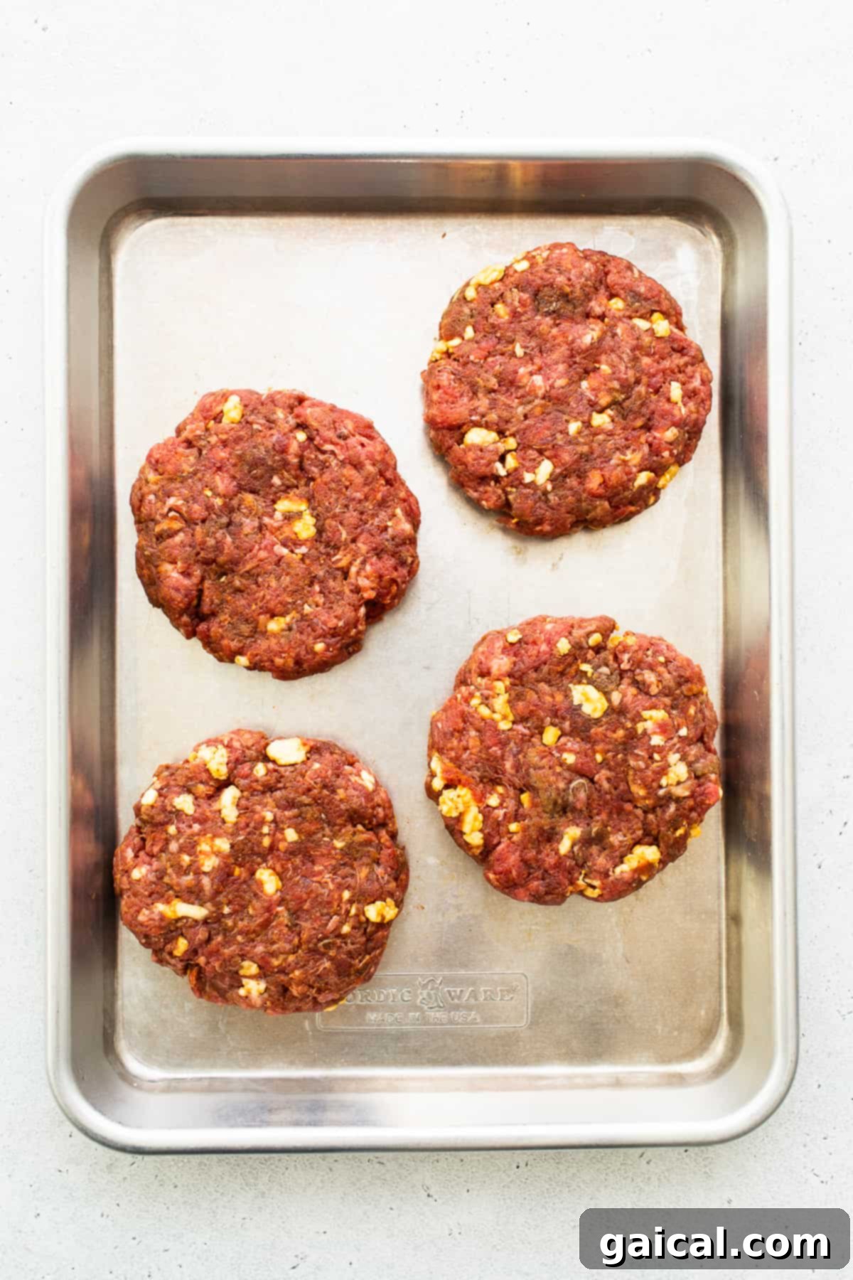 Raw homemade burger patties, perfectly formed and ready for cooking, arranged on a baking sheet.