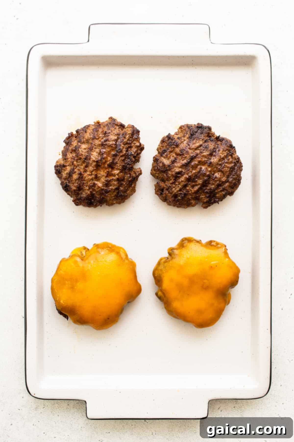 Four perfectly cooked homemade burgers, each topped with a melted slice of cheddar cheese.