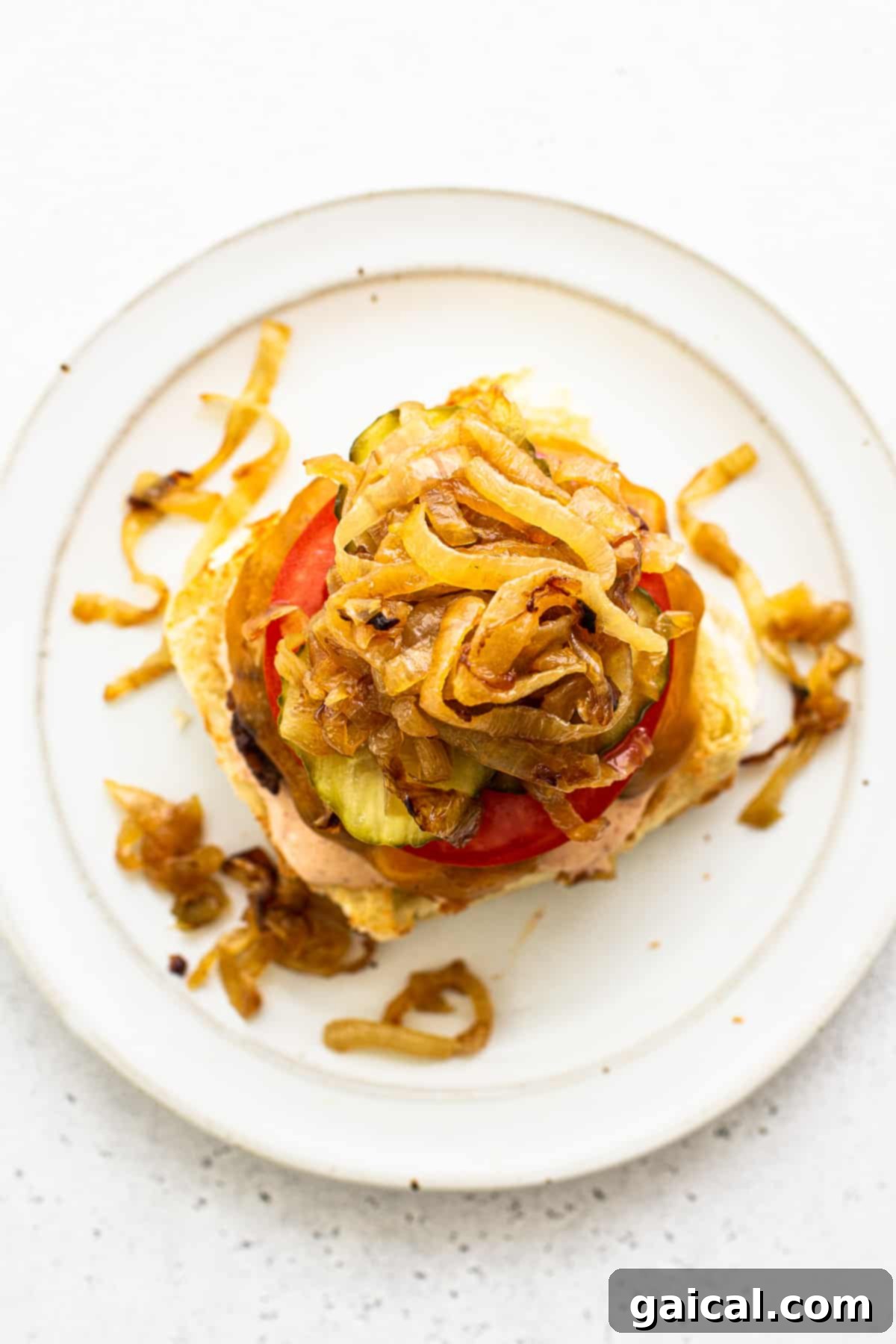 A homemade burger, beautifully assembled and topped with caramelized onions and pickles, presented on a plate.