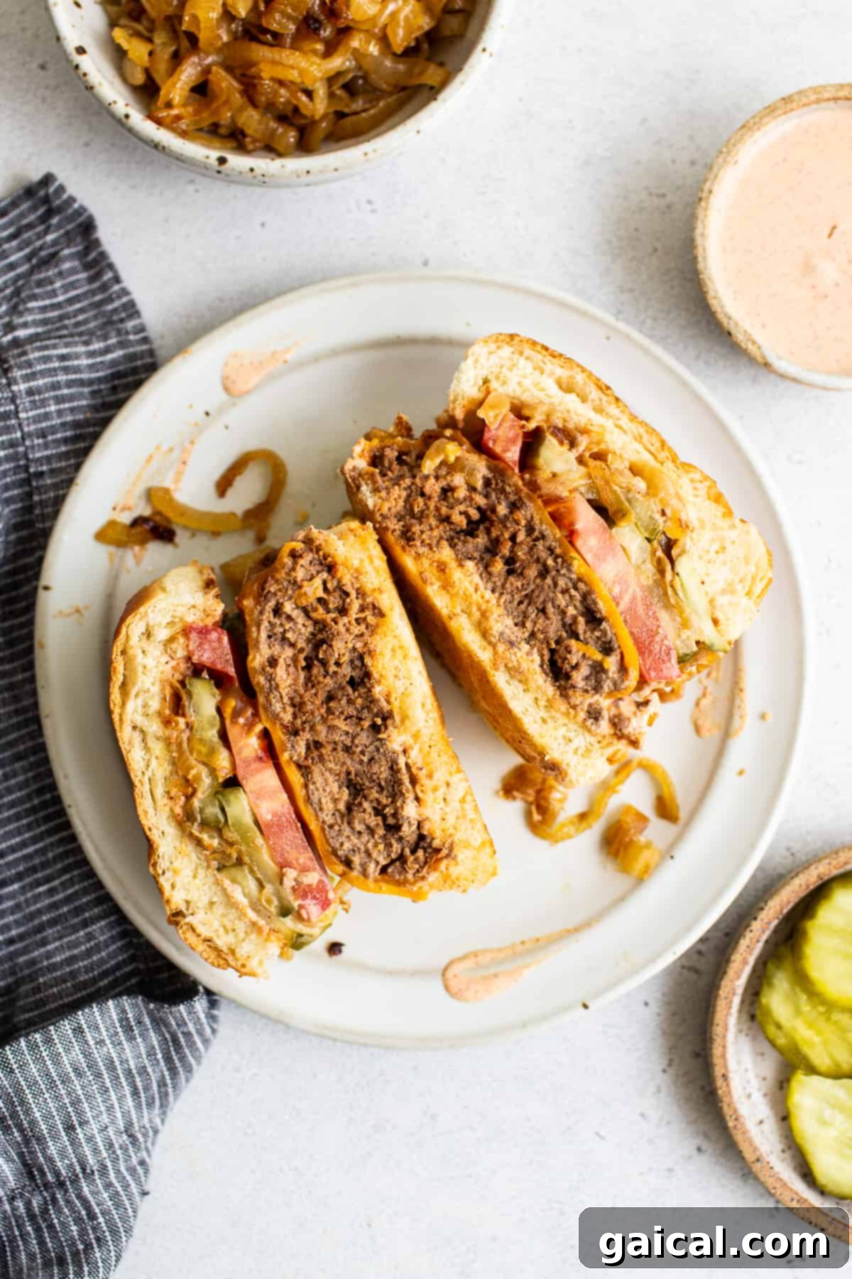 A perfectly cooked homemade burger, sliced in half to show its juicy interior and toppings, on a plate.