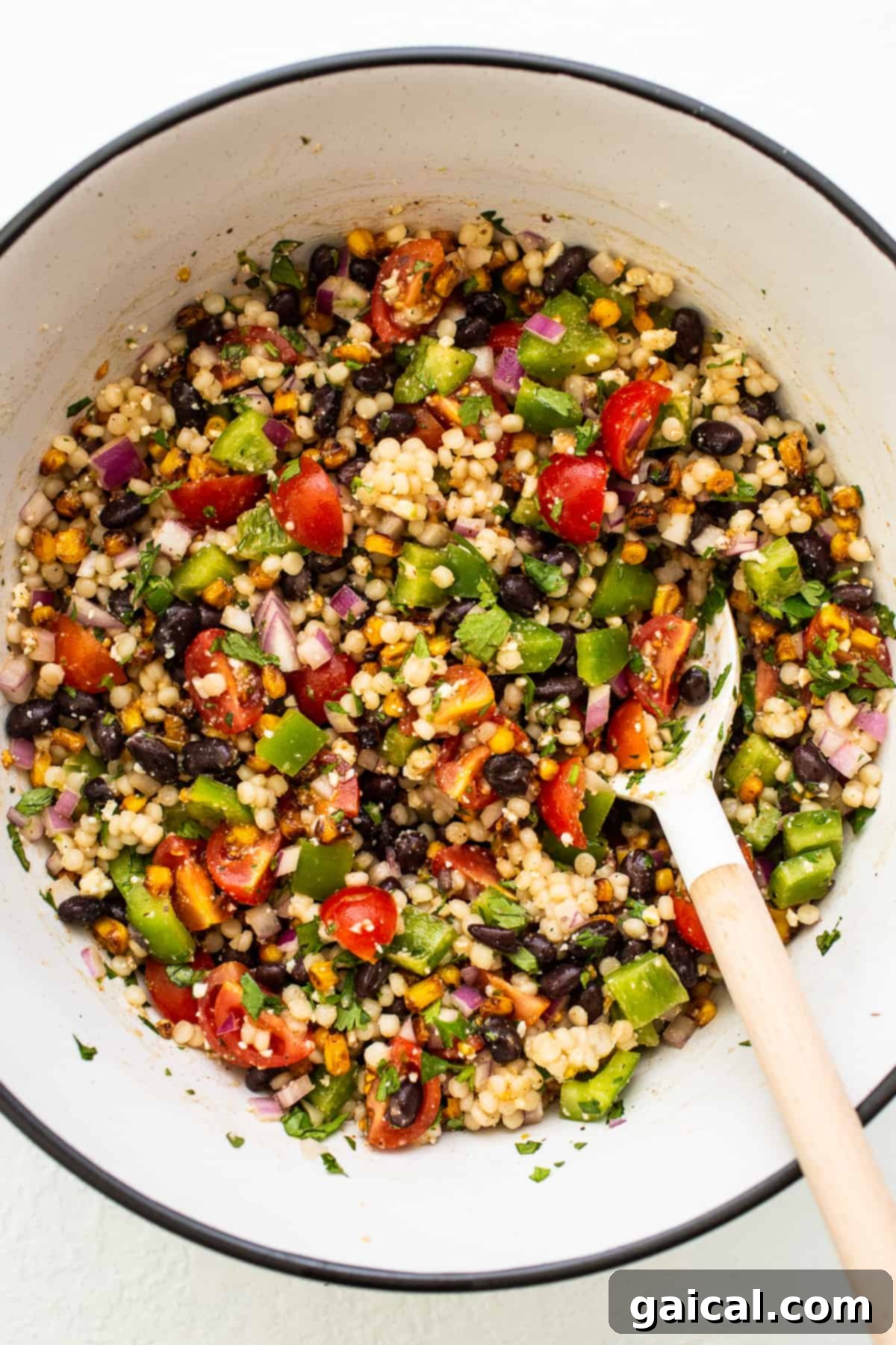 Vibrant Black Bean Couscous Medley 2 A large bowl of vibrant black bean couscous salad, with a serving spoon tucked into the colorful mix of vegetables and grains.