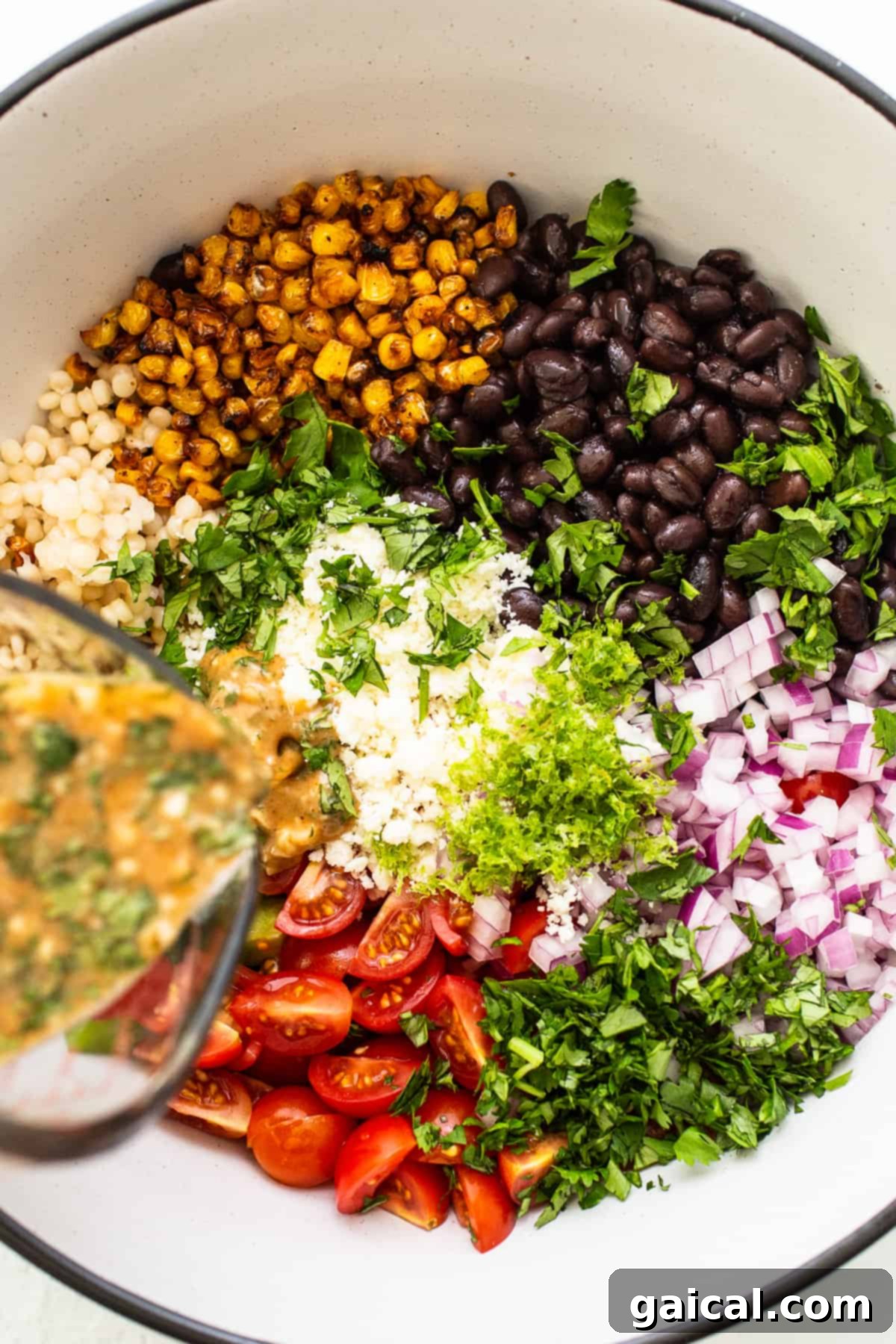 Vibrant Black Bean Couscous Medley 6 Zesty cilantro-lime dressing being poured over a colorful black bean couscous salad in a large bowl, ready for tossing.