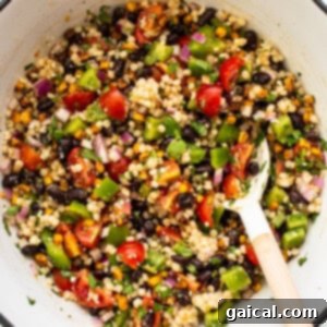 A close-up of a serving of black bean couscous salad in a white bowl, showcasing its colorful ingredients.