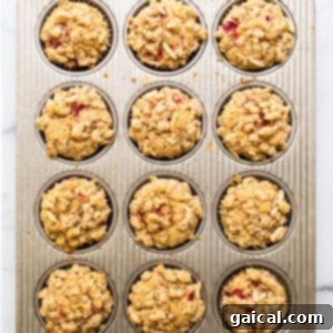 Muffin tin filled with unbaked raspberry muffin batter, topped with streusel, ready for the oven.