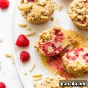 A baked raspberry muffin cut in half, showcasing its fluffy texture and the even distribution of raspberries inside.
