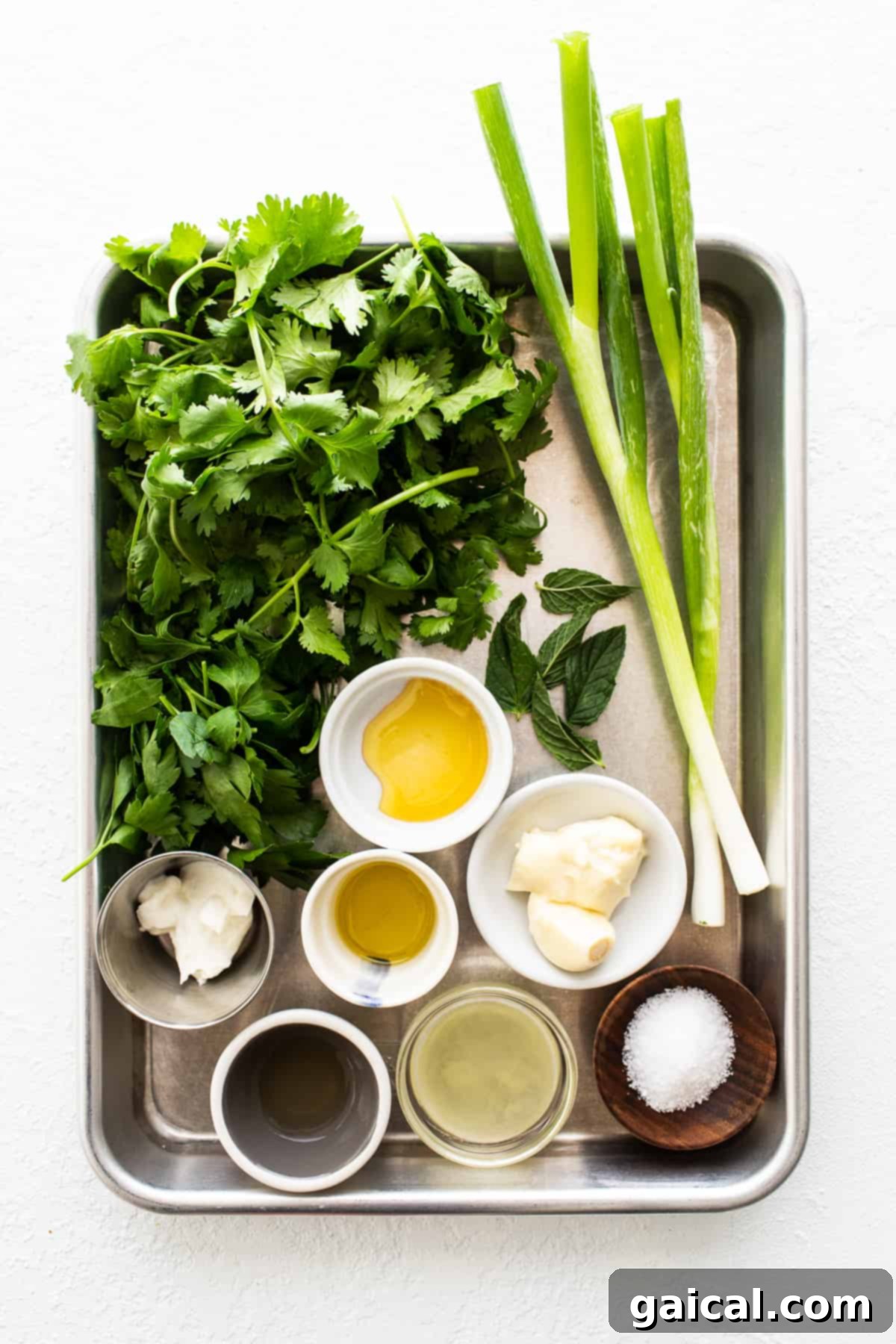 Fresh Ingredients for Green Sauce A selection of fresh ingredients including cilantro, parsley, mint, green onions, garlic, and lemons, beautifully arranged on a baking sheet, awaiting preparation for the green sauce recipe.