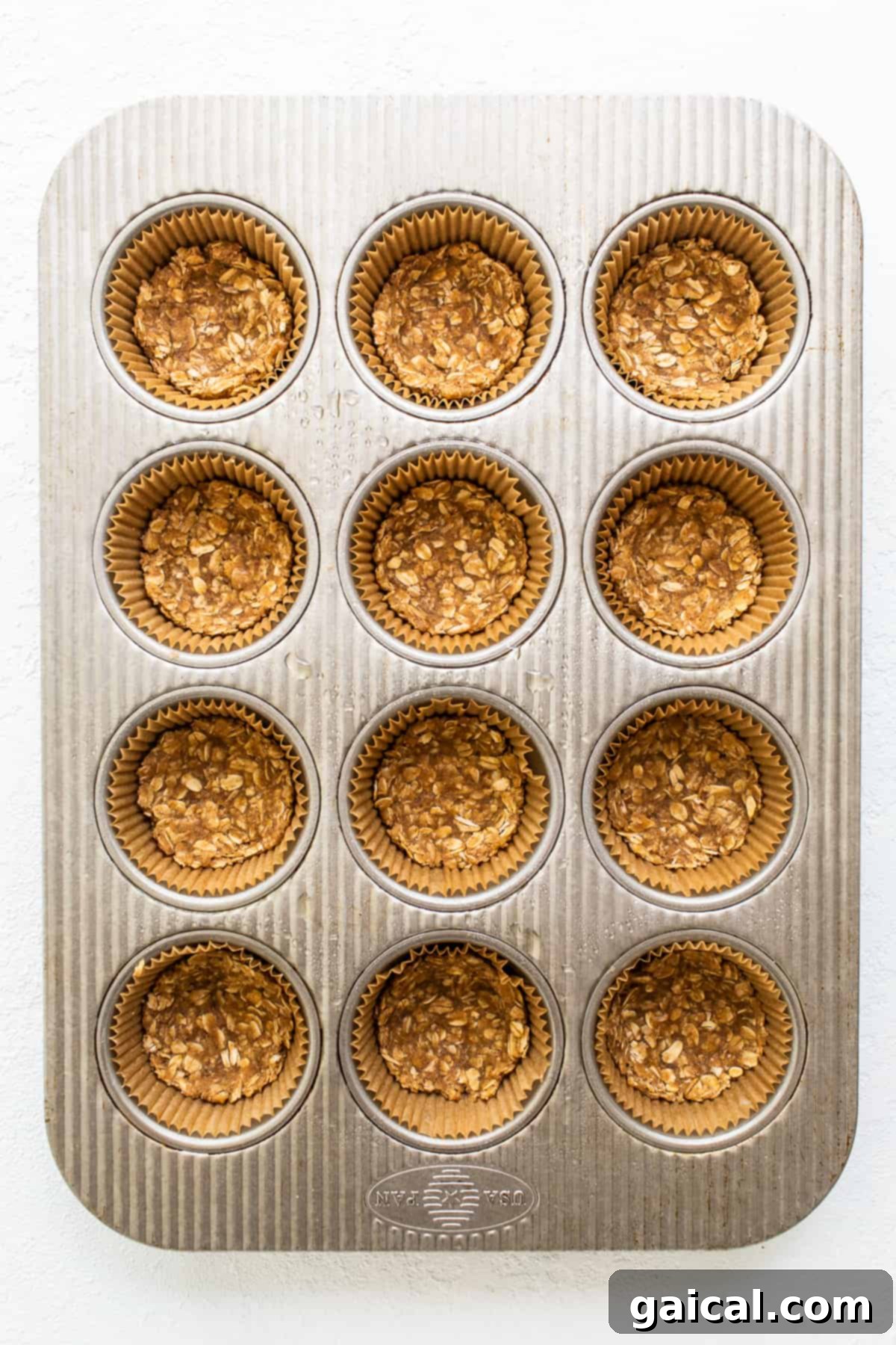 Mini apple crisps are a fun way to serve traditional apple crisps but in a single serving. Top them with vanilla ice cream for the perfect fall dessert. A muffin tin showcasing partially baked crumble crusts, forming the base for the mini apple crisps before the fruit filling is added.