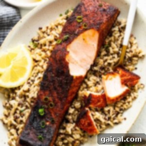 Blackened salmon on a bed of fluffy white rice, garnished with fresh herbs, showcasing its delicious crust.